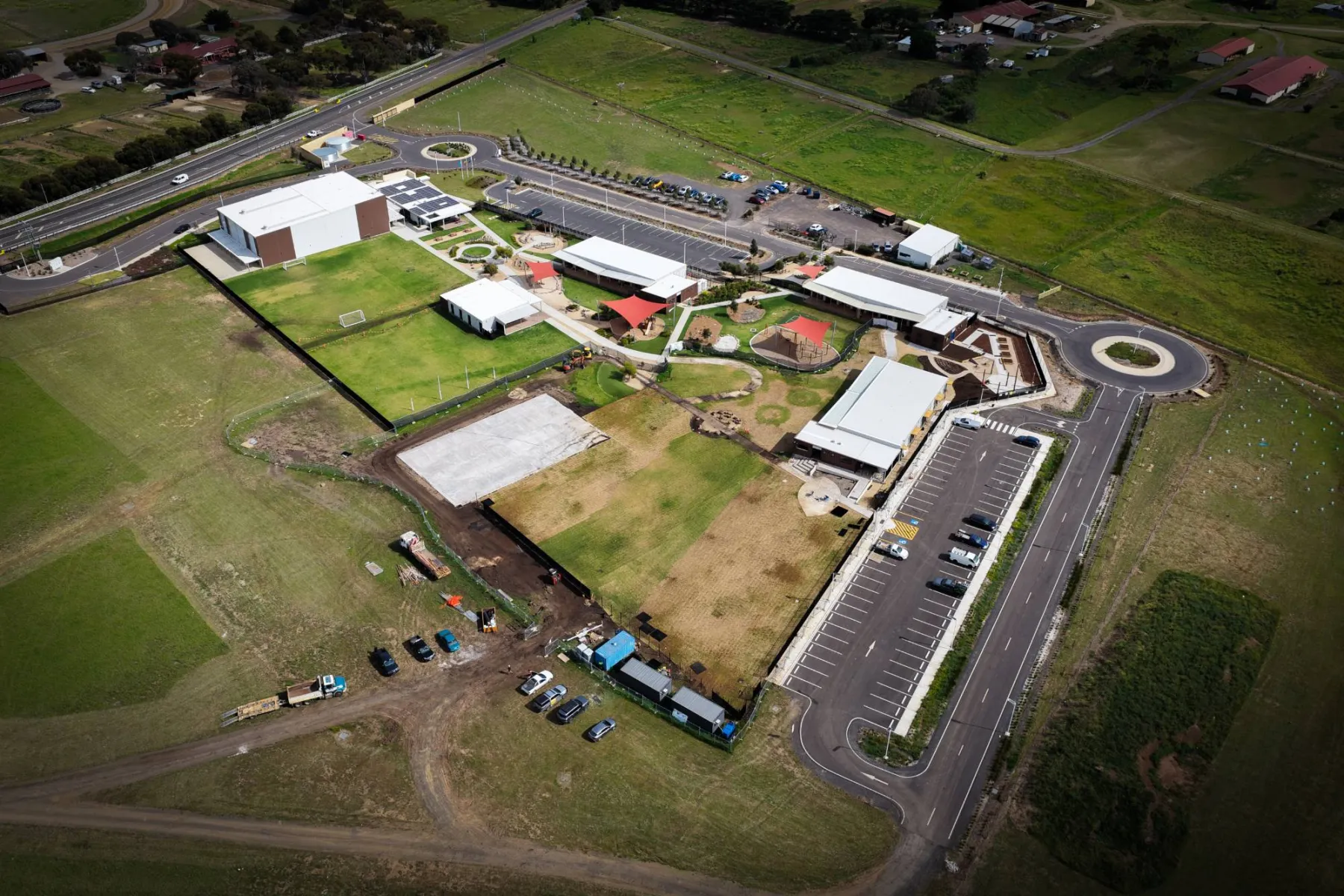 Aerial view of Melton Christian College's Toolern Vale campus: the new building and turfed areas of the expansion alongside the existing school, shade sails over the playgrounds, with farmland beyond
