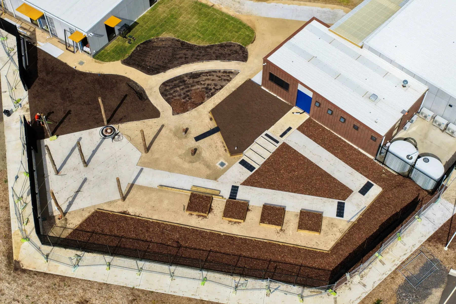 Top-down view of the garden courtyard beside the new building: mulched beds, raised timber planters, compost in the planting areas and a new path