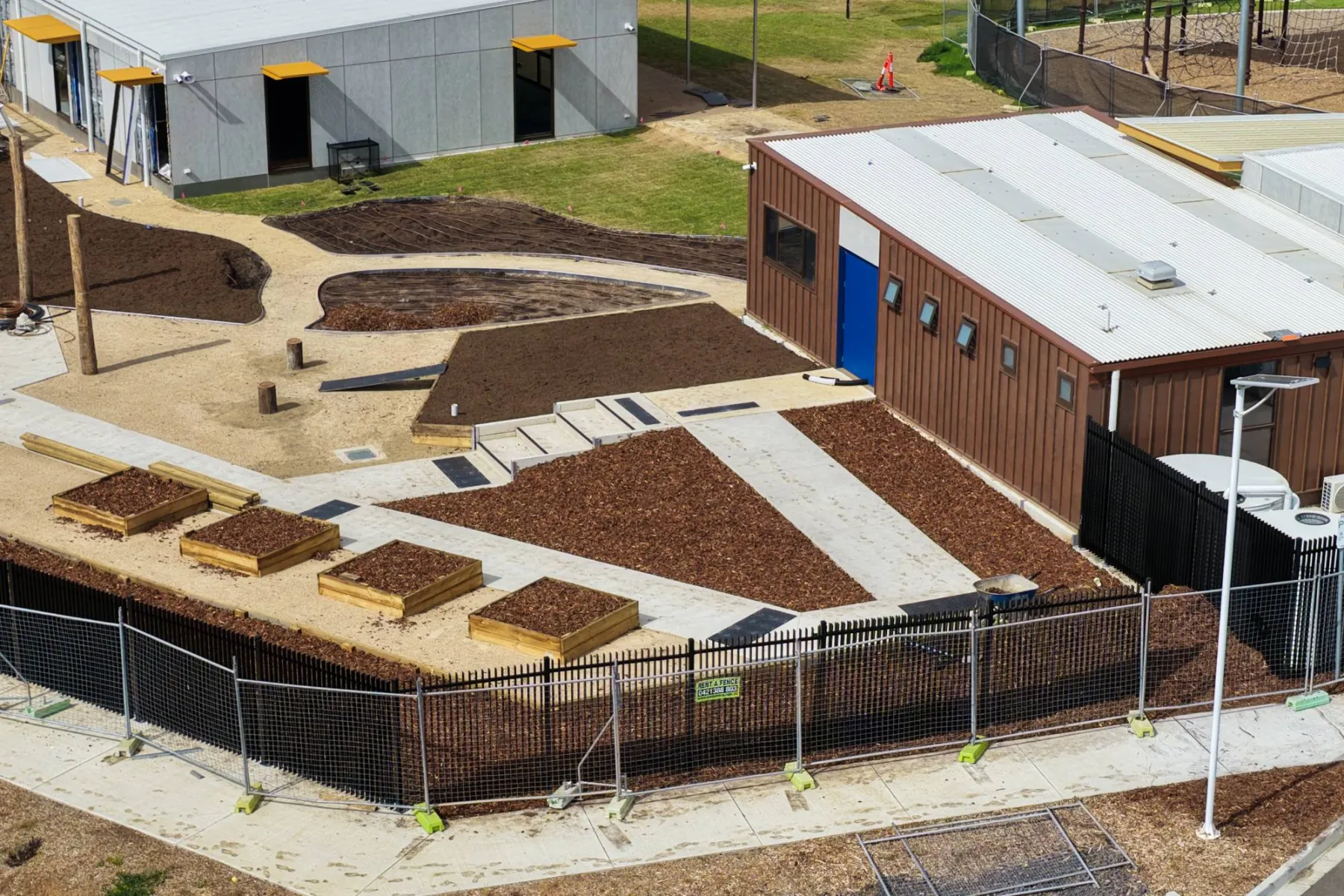 Close view of the courtyard garden beds: mulch, compost-filled raised planters, timber log play posts and the new path and steps